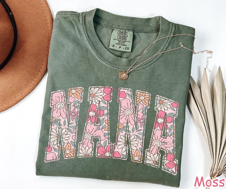 May include: A green t-shirt with a floral design that spells out "NANA". The shirt is made of a soft, comfortable fabric and has a relaxed fit.