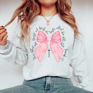 May include: A gray sweatshirt with a pink bow and the text "She is clothed with strength and dignity, she laughs without fear of the future. Proverbs 31:25"