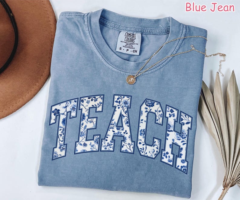 May include: A light blue t-shirt with the word "TEACH" printed in white with a blue and white floral pattern. The shirt is made of a soft, comfortable material.
