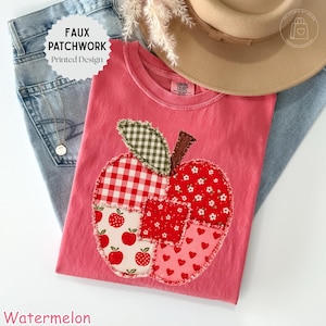 May include: A coral pink t-shirt featuring a faux patchwork apple design. The apple graphic is composed of various fabric patterns including red and white gingham, green and white check, red floral, and red heart prints with frayed edges.