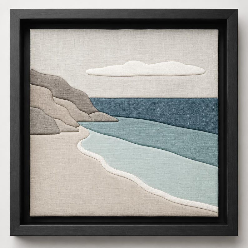 May include: A framed textile art piece depicting a coastal scene. The artwork features a beach with light blue and beige tones, a dark blue ocean, and a light gray sky with a white cloud. The frame is black.