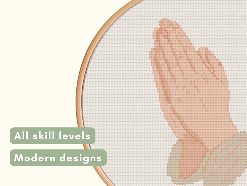 May include: Cross-stitch design featuring hands clasped in prayer, rendered in a pixelated style. The design is set within a wooden embroidery hoop. Text on the left reads "All skill levels" and "Modern designs".