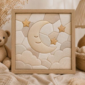 May include: A framed fabric art piece featuring a smiling crescent moon, three stars, and cloud shapes in soft beige and cream tones. The artwork is set against a geometric patchwork background and framed in light wood.