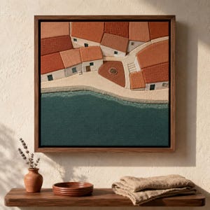 May include: Textured artwork of a coastal village with red-tiled roofs, white buildings, and a teal sea. The artwork is framed in a dark wood. A small brown vase with lavender and a wooden shelf with a bowl and folded cloth are in the foreground.