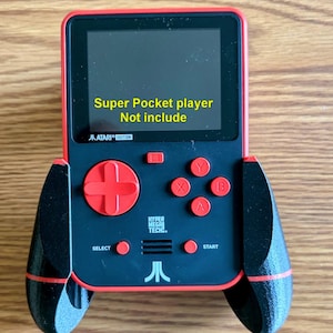 May include: A handheld gaming console with a black and red frame, featuring a screen displaying the text Super Pocket player Not include. The device includes a red directional pad, four red action buttons labelled X, Y, A, B, and Atari branding.