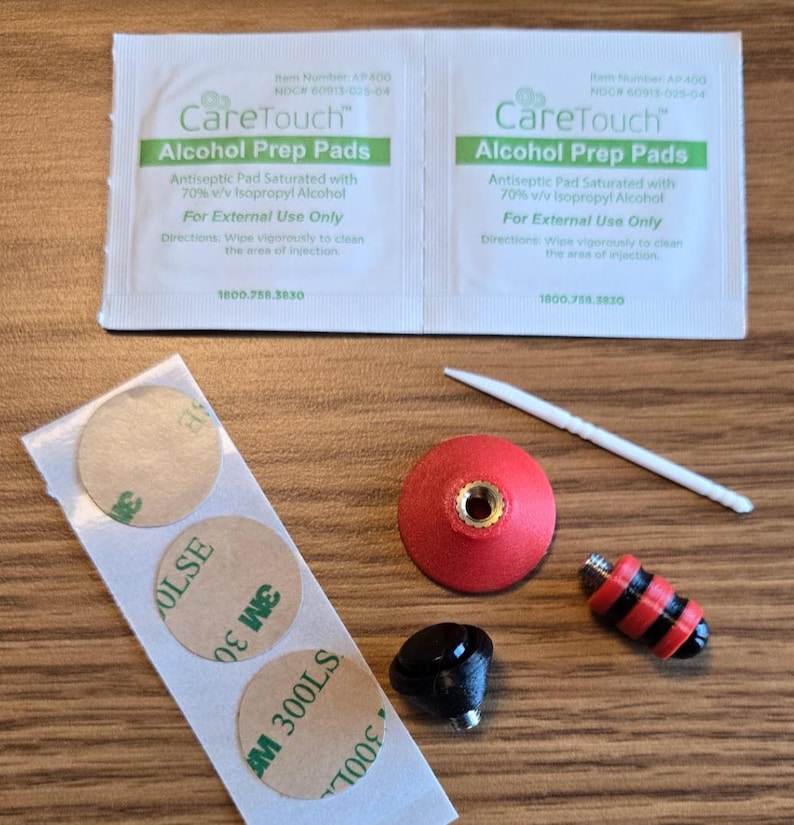 May include: An assortment of medical supplies and accessories, including two "CareTouch Alcohol Prep Pads" packets, adhesive circles, a red and gold object, a black object, a red and black striped object, and a toothpick.