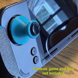 May include: A teal joystick extension cap attached to the analog stick of a dark gray Evercade EXP-R handheld gaming console. The console features a black screen, A and B buttons, and text reading Console game and grip not included.