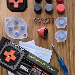 May include: A collection of video game controller parts, including buttons, screws, and a screwdriver. The parts are in various colors, including black, gray, and red. The image also includes a card that says "Controller NOT included" and "SEGA".