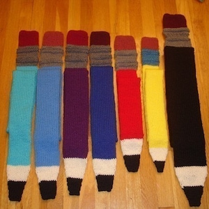 May include: A set of nine knitted pencil-shaped scarves in various colors, including teal, blue, purple, red, yellow, and black.