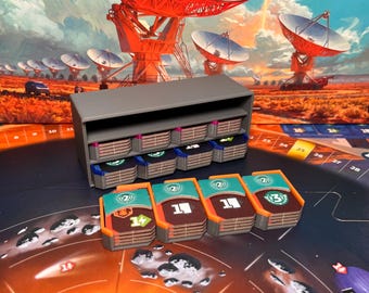 May include: A gray organizer with multiple compartments, filled with game pieces. The game pieces are colorful, with teal, brown, and white designs. The background features a board game with a space theme and a landscape with radio telescopes.