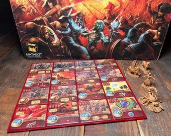 May include: A board game with a red-bordered game board featuring illustrated cards and miniature figurines. The box art depicts a battle scene with figures in armor. The game board has a grid of cards with various illustrations.