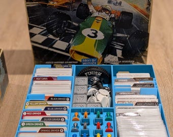 May include: A board game titled "HEAT: Pedal to the Metal" with a box featuring a race car illustration. The game includes various components like cards, driver tokens, and game pieces, all organized in a blue storage container.