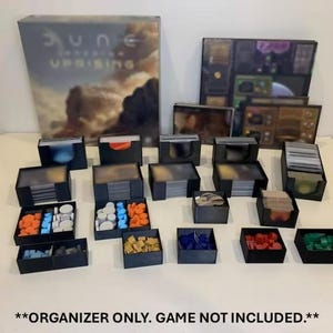 Puede incluir: Un juego de mesa organizador con múltiples cajas y contenedores de almacenamiento negros. El juego incluye cajas para cartas, fichas y otros componentes del juego. La caja del juego "Dune: Uprising" es visible en el fondo. El organizador está diseñado para mantener las piezas del juego organizadas.