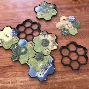 Puede incluir: Un juego de mesa con fichas hexagonales que representan paisajes, incluyendo montañas, bosques y agua. Marcos de plástico negro unen las fichas. Las piezas del juego están dispuestas sobre una superficie de madera.