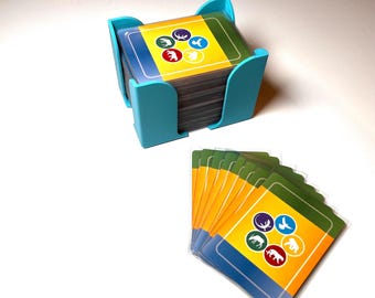 May include: A stack of colorful game cards with animal illustrations, held in a turquoise card holder. The cards have a yellow and green background with images of a deer, bird, and other animals. A few cards are fanned out.