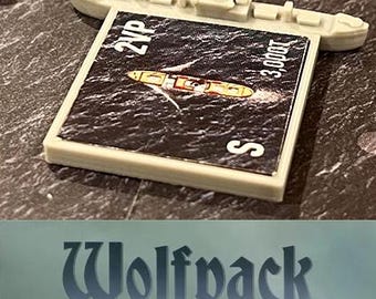 May include: A light gray miniature warship model with a rectangular card featuring a ship illustration on a dark sea. The card has the text "2VP", "3,000T", and the letter "S". The word "Wolfpack" is at the bottom.