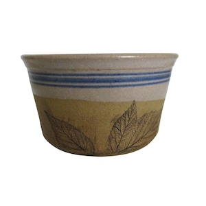 May include: A ceramic bowl with a beige rim and a yellow base. The bowl features two blue stripes and a leaf design. The bowl is approximately 4 inches in diameter and 3 inches tall.