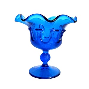 May include: A vibrant blue glass pedestal bowl with a ruffled rim. The bowl has a textured surface and a round base. The stem features a spherical detail. A decorative piece for serving or display.