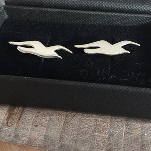 May include: A pair of silver cufflinks in the shape of flying birds, displayed in a black velvet box.