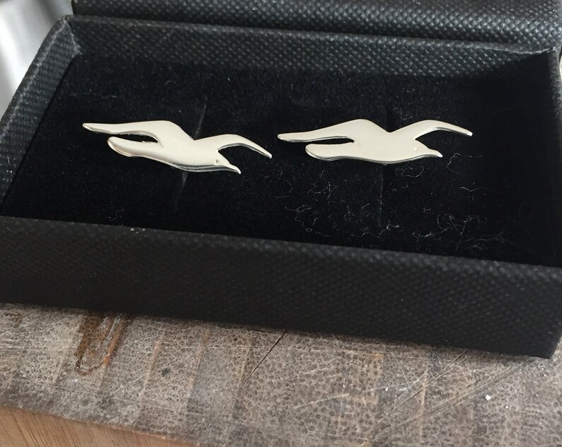 May include: A pair of silver cufflinks in the shape of flying birds, displayed in a black velvet box.