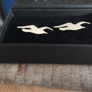 May include: Two silver cufflinks in the shape of flying birds, displayed in a black velvet box.