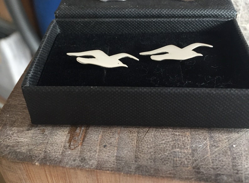 May include: Two silver cufflinks in the shape of flying birds, displayed in a black velvet box.