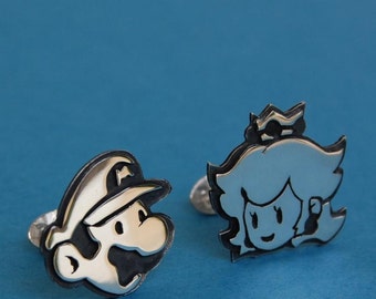 May include: A pair of silver cufflinks featuring cartoon characters from the video game Super Mario Bros. One cufflink features Mario, the other features Princess Peach.