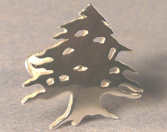 May include: A silver-coloured metal pendant shaped like the Cedar of Lebanon tree, a national symbol of Lebanon.
