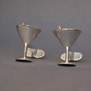 May include: A pair of silver martini glass cufflinks. The cufflinks are made of polished silver and feature a detailed martini glass design.