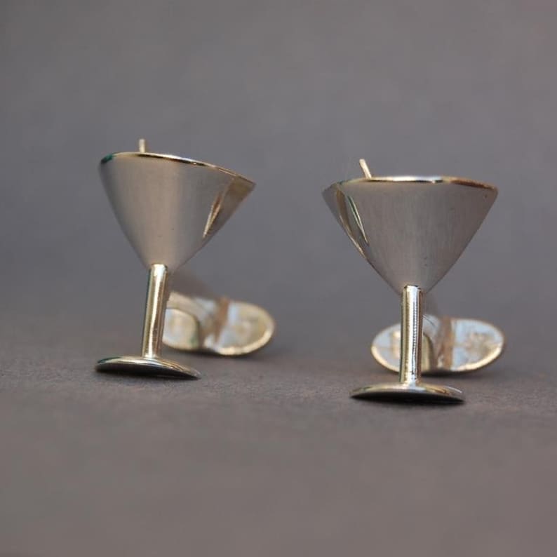 May include: A pair of silver martini glass cufflinks. The cufflinks are made of polished silver and feature a detailed martini glass design.