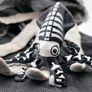 Puede incluir: Figura de calamar en blanco y negro con diseño de esqueleto. El calamar tiene un cuerpo negro con detalles de costillas blancas y tentáculos blancos. La figura está sobre un fondo oscuro y texturizado.