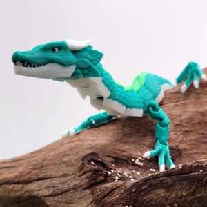 Könnte beinhalten: Eine teal- und weiße, artikulierte Drachenfigur mit einem grünen Streifen auf dem Rücken, die auf einem braunen Ast posiert.
