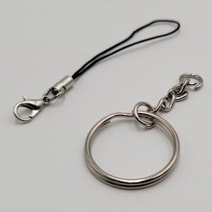 May include: A silver key chain with a round ring and a chain attached to a silver hook. A black string lanyard with a silver hook is also included.