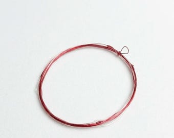 May include: A circular coil of red and white fishing line, with a small loop tied at one end. The line is thin and appears to be made of a synthetic material. The background is plain white.