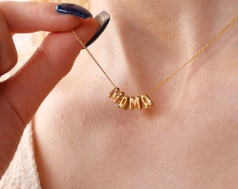 May include: A gold necklace with the word "MOMMA" spelled out in individual letters. The letters are connected by a thin gold chain.