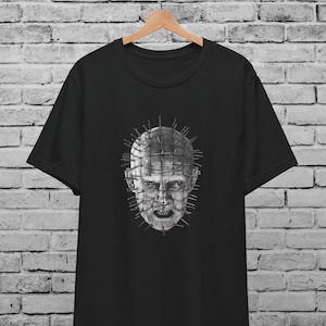 May include: Black t-shirt with a graphic print of a character from the horror movie Hellraiser. The character has a head covered in nails and a menacing expression.