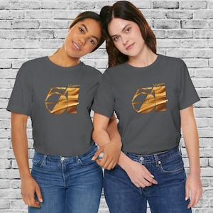 May include: Two people wearing charcoal gray t-shirts with a gold Studio 54 logo printed on the front. The logo is a stylized number 54 with a gold, wavy texture.
