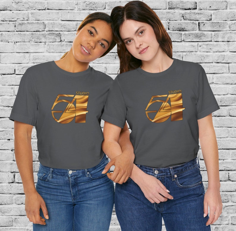 May include: Two people wearing charcoal gray t-shirts with a gold Studio 54 logo printed on the front. The logo is a stylized number 54 with a gold, wavy texture.