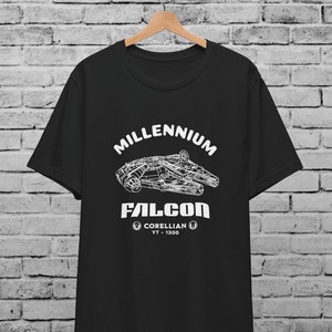 Puede incluir: Camiseta negra con un gráfico blanco del barco espacial Millennium Falcon. El texto "Millennium Falcon" está por encima del barco espacial, y el texto "Corellian YT-1300" está por debajo del barco espacial.
