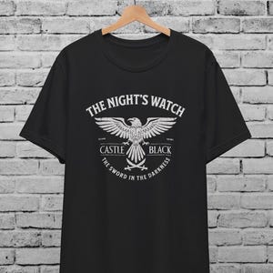 以下が含まれることがあります： 黒いTシャツに、白い鷲のグラフィックと「The Night's Watch」、「Castle Black」、「The Sword in the Darkness」の文字がプリントされています。