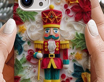 May include: A phone case with a 3D design of a nutcracker soldier. The case has a white background with red, yellow, and green floral accents. The nutcracker is dressed in a red coat, blue trousers, and a gold crown. The case is held in front of a festive background.