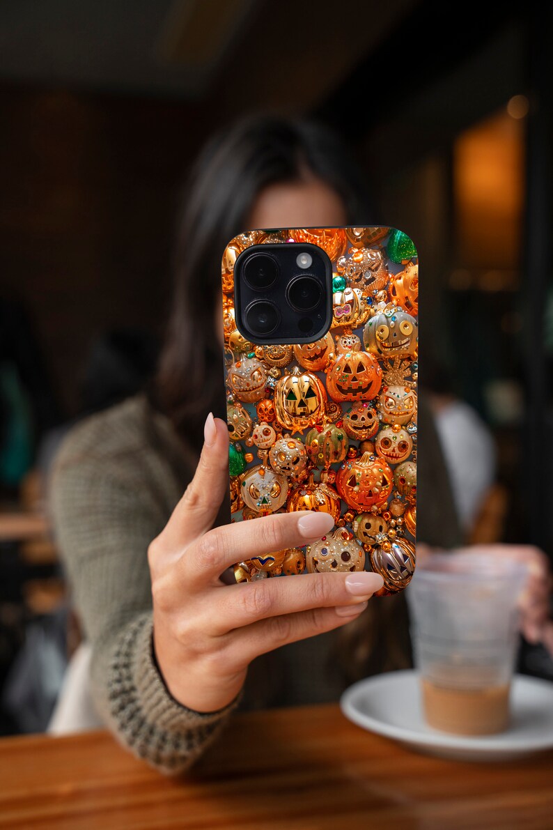 May include: A black iPhone case with a pattern of gold and orange jack-o'-lantern ornaments.