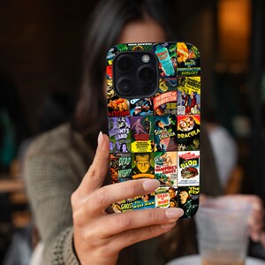 Puede incluir: Una funda de tel&eacute;fono negra con un collage de carteles de pel&iacute;culas de terror vintage. Los carteles incluyen t&iacute;tulos como "La novia de Frankenstein", "El hijo de Dr&aacute;cula", "The Blob" y "El fantasma y el hombre lobo".