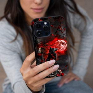 May include: A black phone case with a wolf howling at a red moon in a dark forest. The case has a black background with red and white accents.