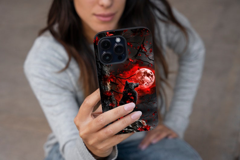 May include: A black phone case with a wolf howling at a red moon in a dark forest. The case has a black background with red and white accents.
