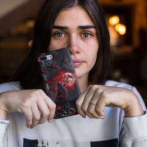 May include: A black phone case with a red and black wolf howling at a full moon in a dark forest scene.