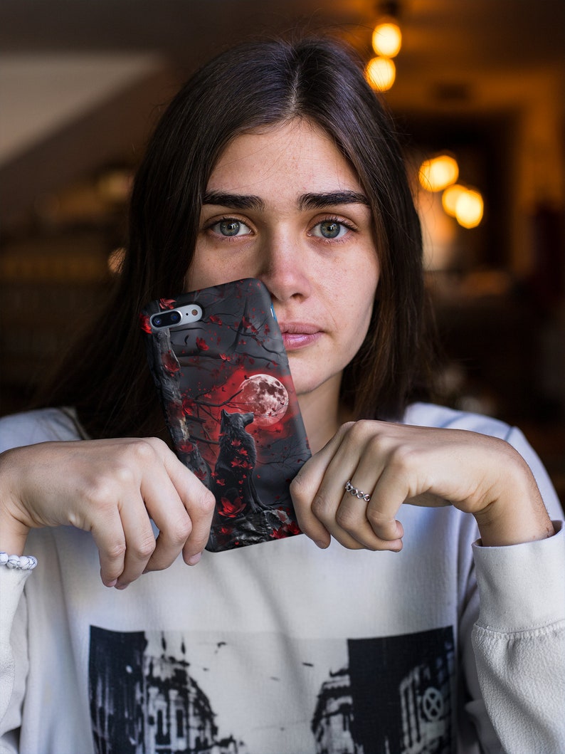May include: A black phone case with a red and black wolf howling at a full moon in a dark forest scene.