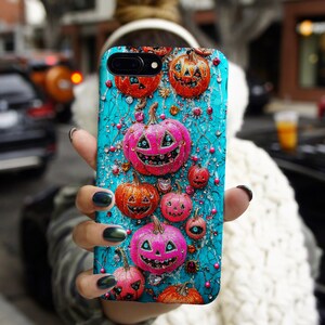 May include: A teal phone case featuring a Halloween-themed design. The case is adorned with orange and pink jack-o'-lanterns, sparkling gems, and decorative vines. The pumpkins have smiling faces and are of varying sizes, creating a festive and eye-catching accessory.