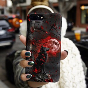 May include: A black phone case with a wolf howling at a red moon in a dark forest. The wolf is surrounded by red flowers and leaves.