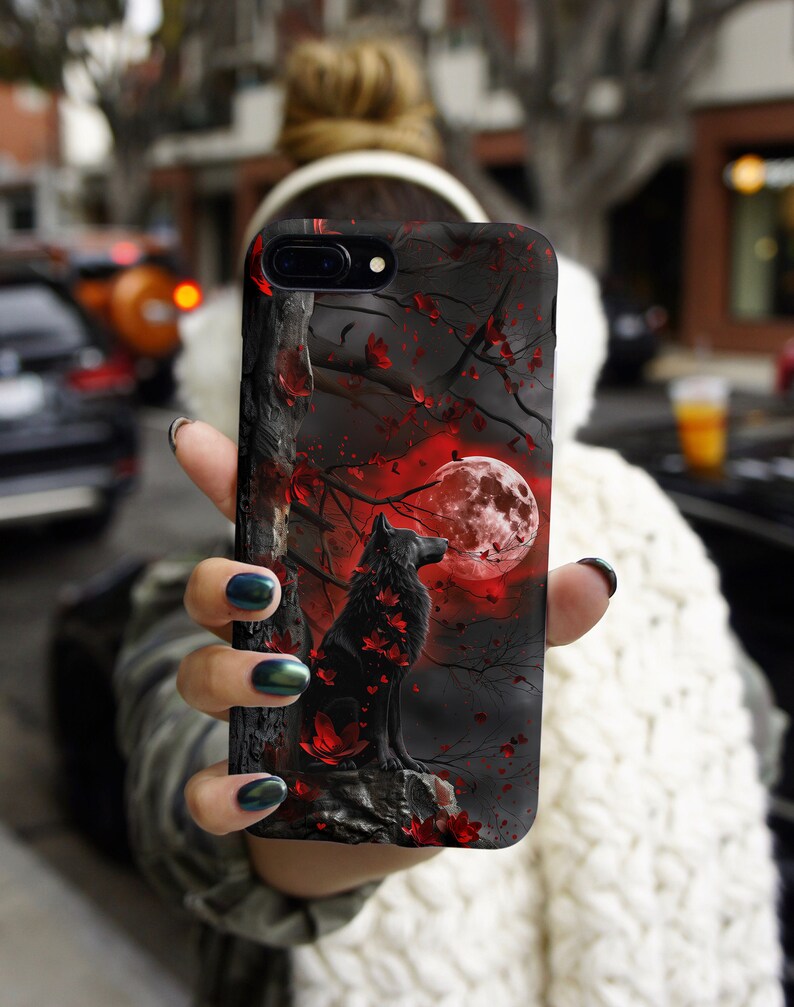 May include: A black phone case with a wolf howling at a red moon in a dark forest. The wolf is surrounded by red flowers and leaves.